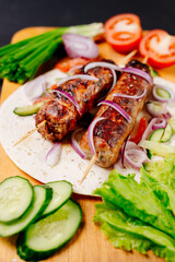 Grilled lula kebab on pita bread with vegetables on a dark background