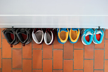 Row of used shoes lined up partially under shoe cabinet inside apartment top view