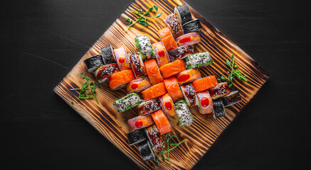 set of sushi roll with salmon, avocado, cream cheese, cucumber, rice, caviar, eel, tuna in wooden plate on black background