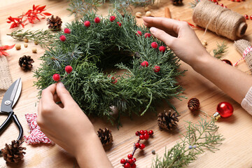 Florist making beautiful Christmas wreath with berries at wooden table, closeup © New Africa