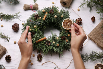 Florist making beautiful Christmas wreath at white wooden table, top view