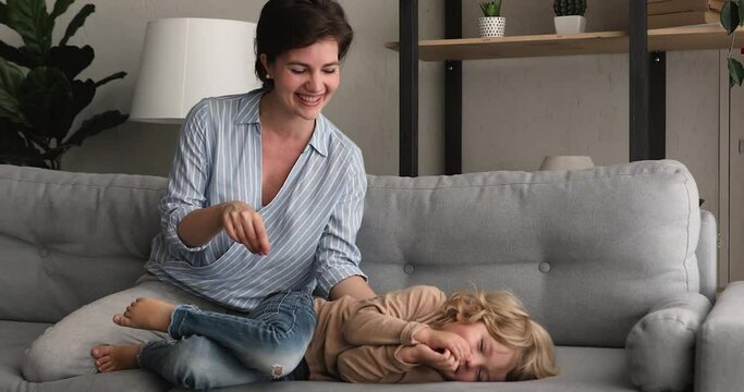 Young pretty mother play with cute little son at home, fooling lying on sofa in living room laughing tickling boy, feels happy spend time with preschool kid. Family leisure, weekend activity concept