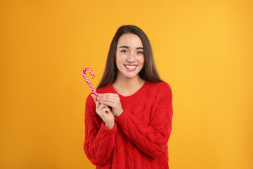 Young woman in red sweater holding candy cane on yellow background. Celebrating Christmas