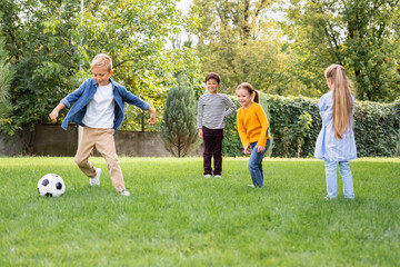 Obraz premium Positive multiethnic children standing near friend playing football in park