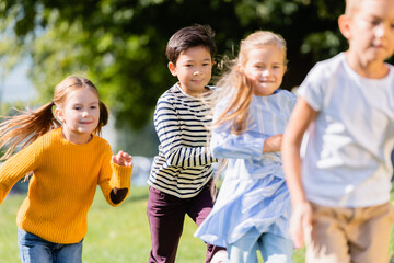 Smiling multiethnic children running near friends on blurred foreground outdoors