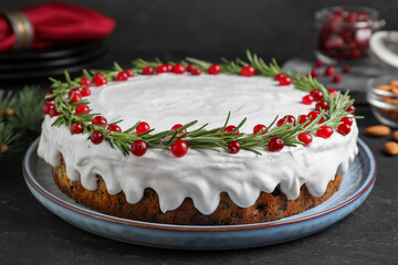 Traditional Christmas cake decorated with rosemary and cranberries on dark grey table, closeup