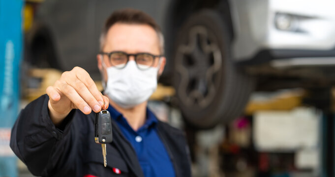 Car Maintenance And Automobile Service Garage. Portrait Beard Male Manager Give A Car Key To Camera And Wearing Medical Face Mask Protection Coronavirus.