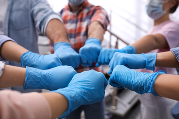 People in blue medical gloves joining fists indoors, closeup