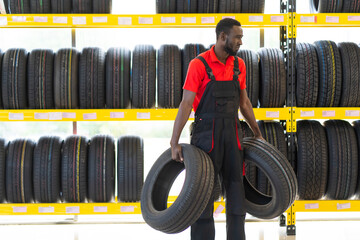 Black male Mechanic holding a tire and showing wheel tires at car repair service and auto store...