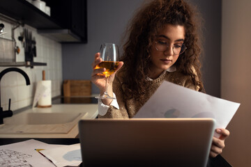 Portrait of young woman working at home in kitchen using laptop.
