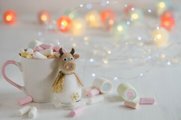 White cup with marshmallows and a toy bull on a blurred background.