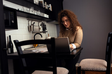 Portrait of young woman working at home having video call at kitchen using laptop.