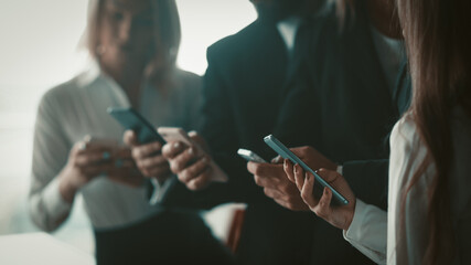 Obraz premium Business people using mobile phones together standing in office. Close up shot of human hands holding smartphones. Blurred image. Selective focus on female hand in foreground.