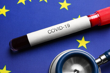 Stethoscope and test tube with blood sample on European Union flag background, closeup. Coronavirus...