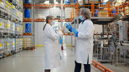 Mature man and woman wearing safety mask, gloves and lab coat standing at chemical manufacturing