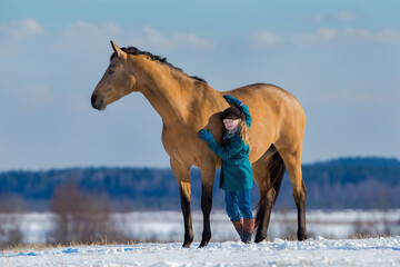 Young cute girl hugs Trakehner buskin horse outdoor in winter background. One child and big mare standing on a hill in winter