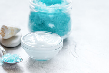Fototapeta na wymiar blue bath salt, body cream and shells for spa on white table background