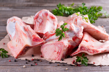 Fresh beef bone on wooden background with vegetables and herbs on the background