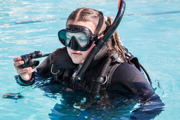 Scuba dive training in a pool, a student with a wetsuit and dive mask on and regulator in her hand close up.