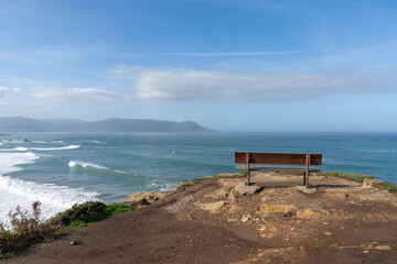 Fototapeta na wymiar scenic viewpoint with wooden bench on beautiful ocean coast with high cliffs and big waves