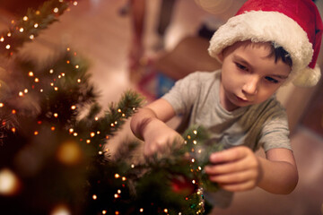 A little kid focused on ornamenting a Christmas tree at home. Together, New Year, family, celebration