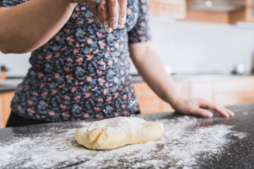 Woman sprinkling dough with flour in kitchen.