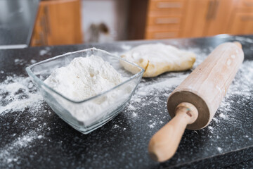 Fototapeta na wymiar White flour in glass bowl, wooden roller and dough in the kitchen ready for rolling.