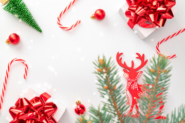 Surprise gift. White gift box with red ribbon, New Year balls and sparkling lights in Christmas composition on white background for greeting card. Flat lay, top view, copy space.