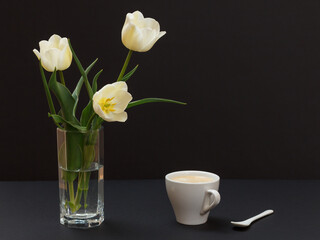 Bouquet of yellow tulips in vase with cup on a black background.