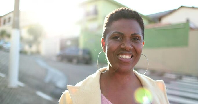 African woman standing outside smiling with sunflare. Black ethnicity lady looking at camera in street