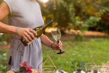 Anonymous woman pouring a glass of white wine at a relaxed garden party. - obrazy, fototapety, plakaty