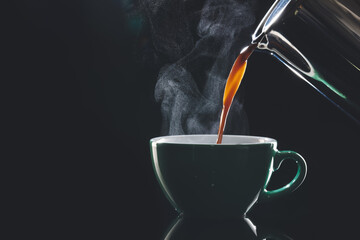 Pouring of hot coffee in cup on dark background