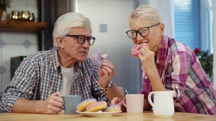 Happy senior couple talking and eating breakfast in kitchen