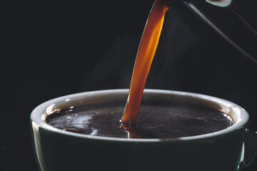 Pouring of hot coffee in cup on dark background, closeup