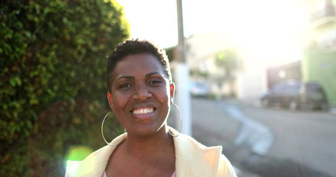 African woman standing outside smiling with sunflare. Black ethnicity lady looking at camera in street