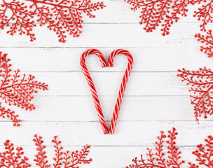 Heart shape made of candy canes on white wooden planks with red glitter branches framing. Christmas concept.