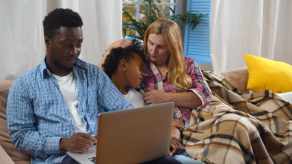 Modern diverse parents and sick son sitting at couch and speaking with online doctor at home