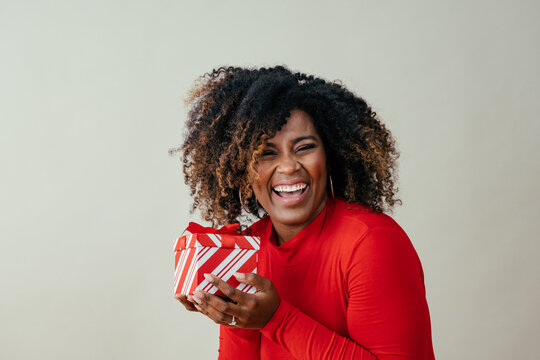 Portrait of a happy mid woman laughing and holding red Christmas gift box