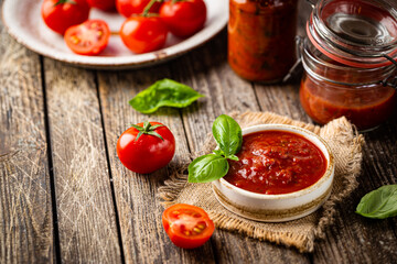 Bowl of italian tomato sauce with basil and fresh tomatoes on wooden background