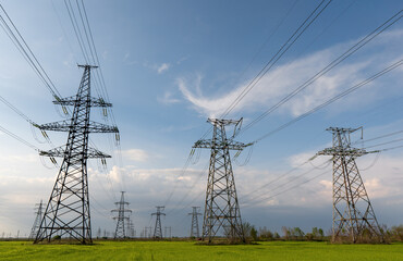 High voltage lines and power pylons and a green agricultural landscape on a sunny day.
