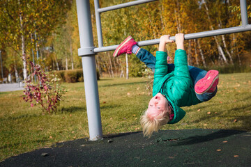 Happy cute little girl upside down on monkey bars