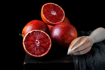 Blood oranges and wooden squeezer on the table against the black background. Low key photo