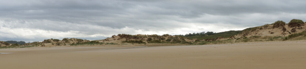 panorama of an empty beach with tall sand dunes under an overcast sky