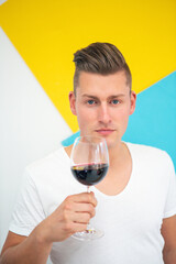 blond man holding a glass of red wine on colorful background