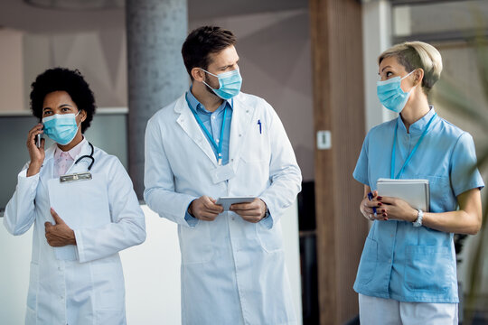 Healthcare Workers With Face Masks Talking While Walking Through A Hallway At The Hospital.