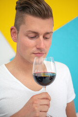 blond man holding a glass of red wine on colorful background