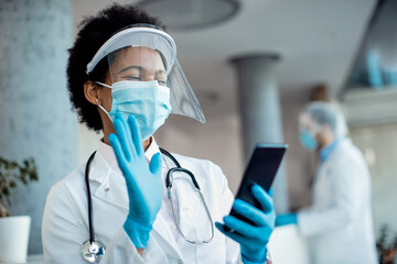 Happy black doctor making video call over smart phone while working at the clinic during COVID-19 pandemic.