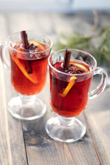 Two cups with mulled wine on wooden table with blur snow and branch of Christmas tree. Concept...