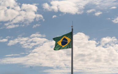 Brazilian flag flying and in the background the blue sky with white clouds