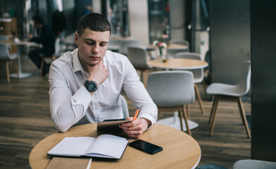 Pensive businessman watching tablet while sitting leaned on hand in cafe